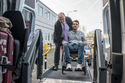 professional driver assisting man on wheelchair to board hydraulic lift van